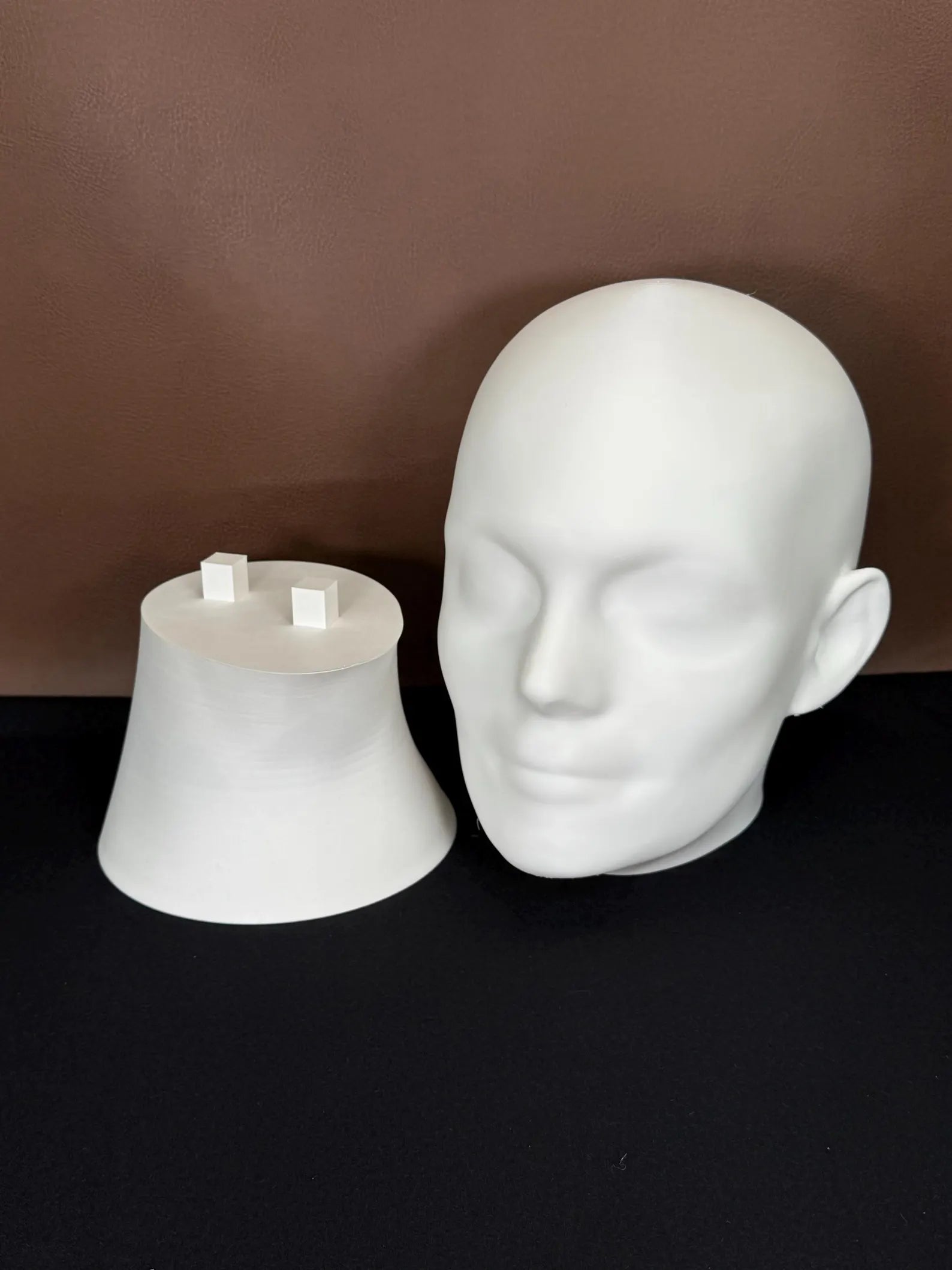 White 3D printed head in 2 pieces on a dark surface with a brown background