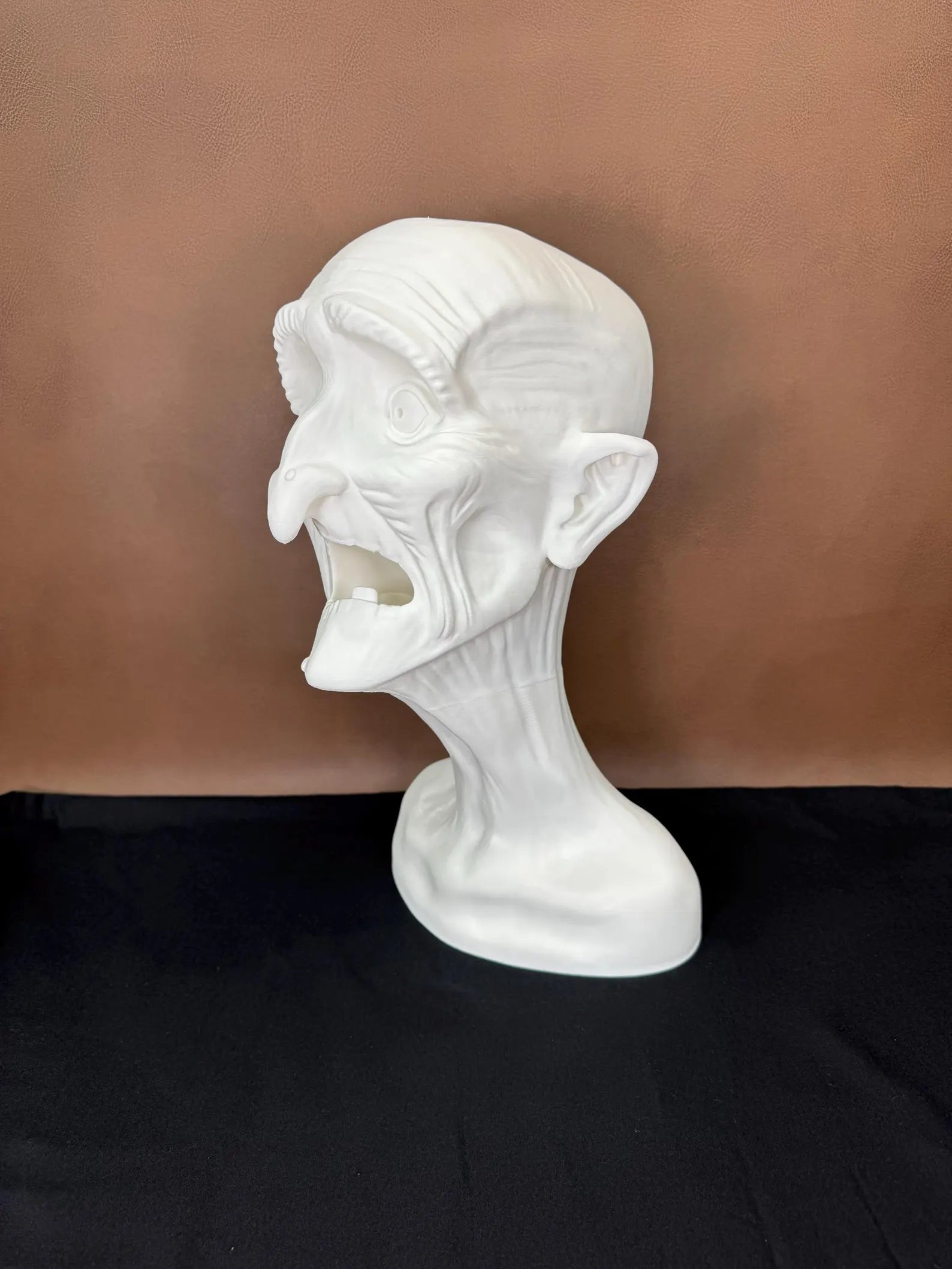 White 3D printed head sculpture with exaggerated features on a brown background