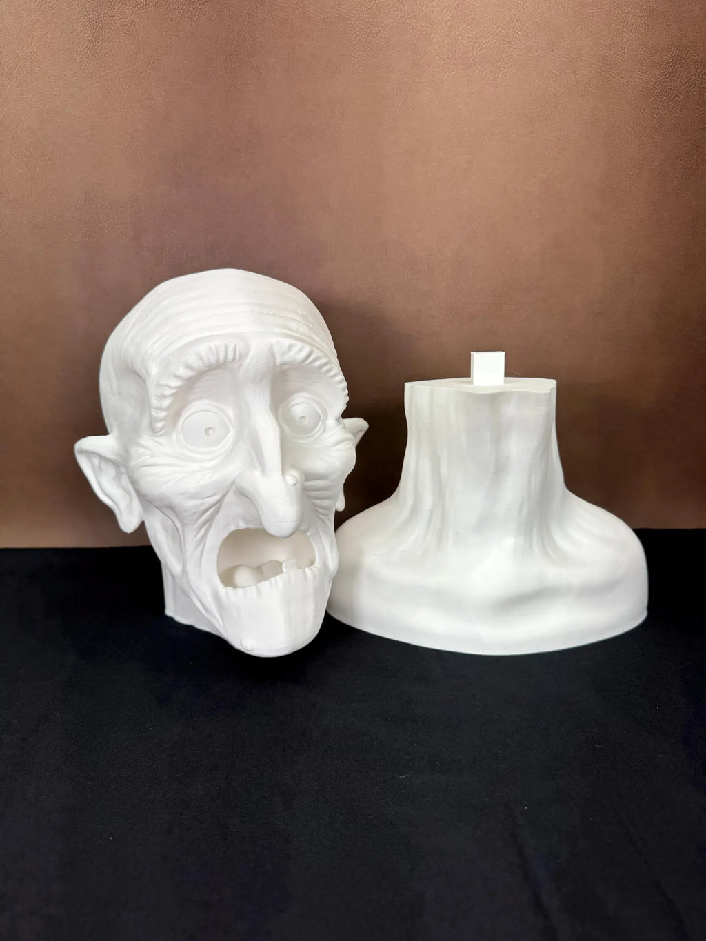White 3D printed head sculpture in 2 pieces with exaggerated features on a brown background